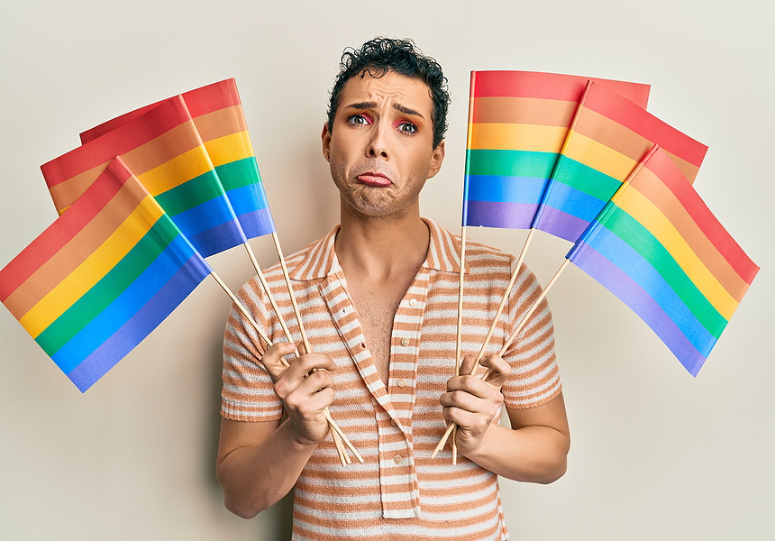 Sad LGBTQ man holding pride flag.
