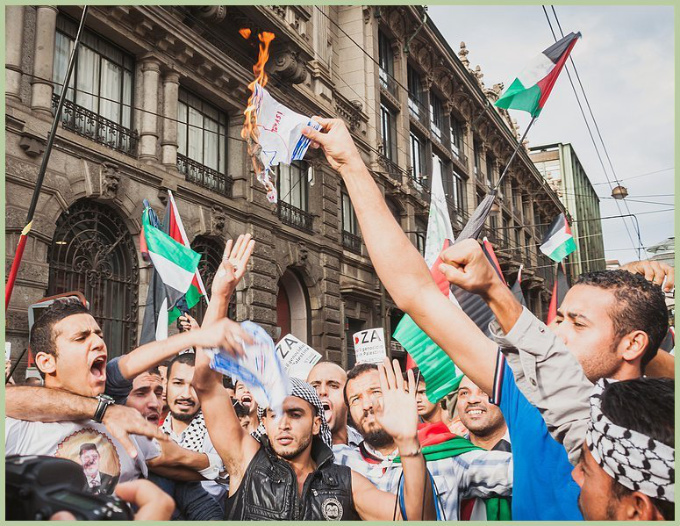 Pro-Palestinian protesters burning a drawing of an Israeli flag.